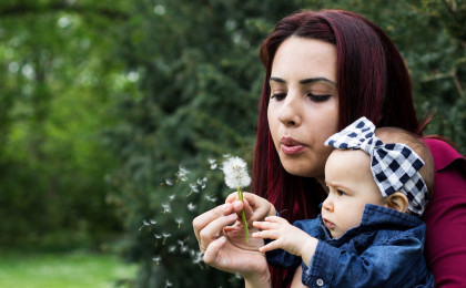 Lady Holding Baby Blowing Dandilion