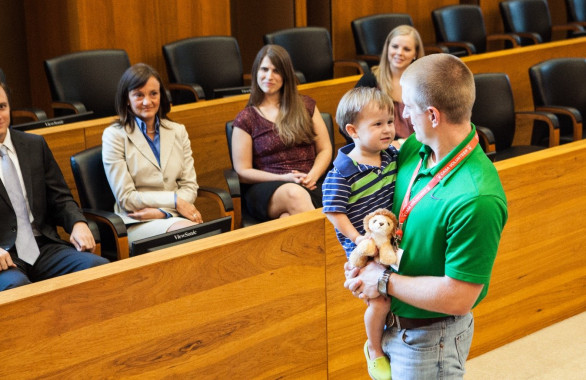 Man Holding Small Child in Court Room With Jury Looking on